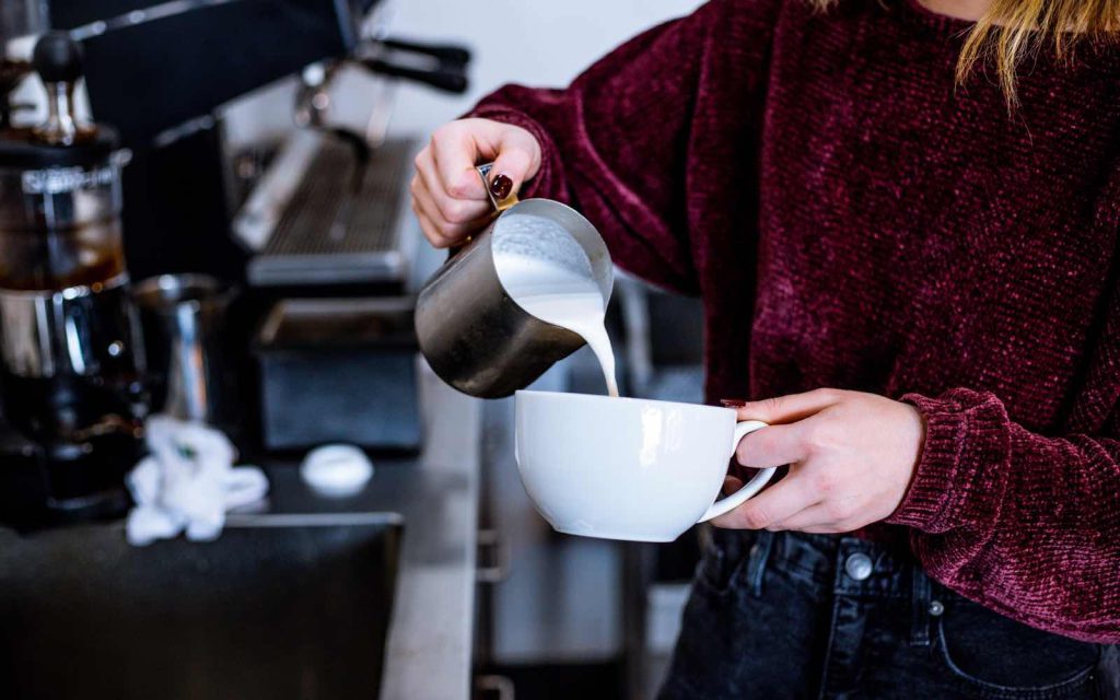 Barista gibt Milch in Tasse